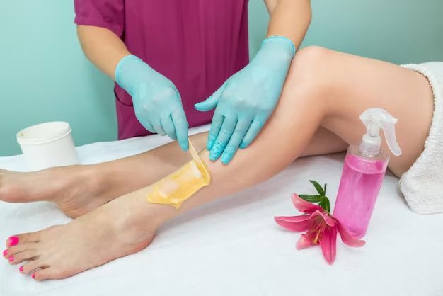 Beautician performing leg waxing treatment on woman using warm wax strip in professional beauty salon